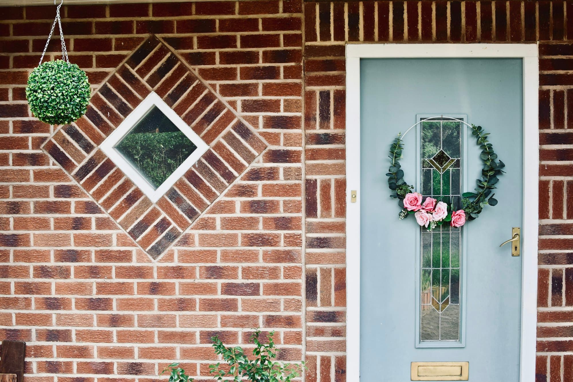 A pale front door with a wreath on a brick house