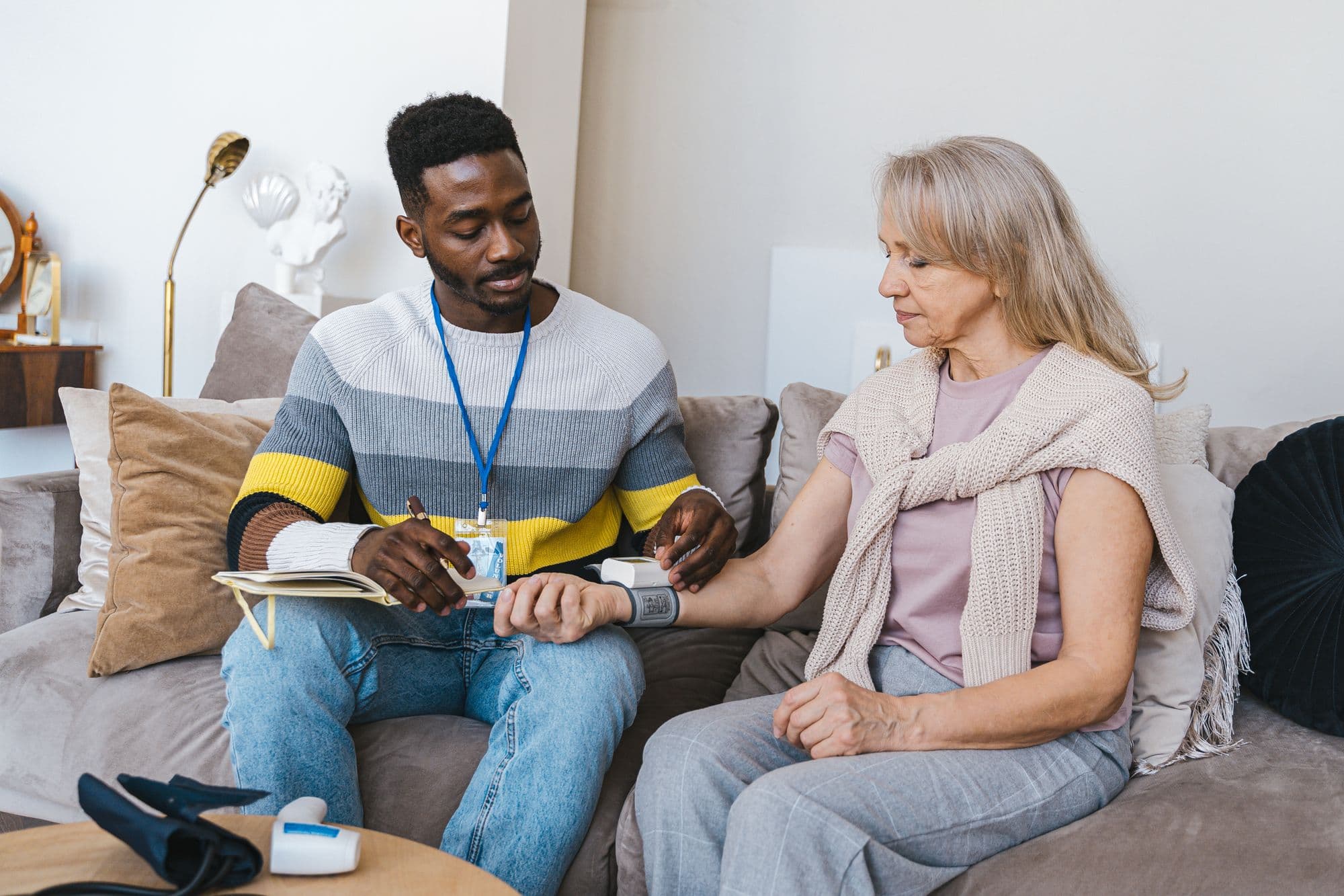 A care worker checking an older woman’s blood pressure during a home visit